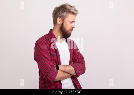 Portrait de côté de jeune barbu déprimé en rouge chemise bras pliants et regardant côté, souffrant de mélancolie, dépression.Prise de vue en studio isolée sur fond gris Banque D'Images