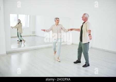 Heureux couple senior apprenant à danser devant le grand miroir dans le studio de danse Banque D'Images