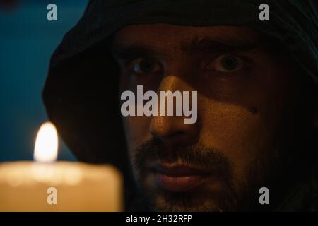 Gros plan sur le visage d'un homme non rasé dans une capuche noire sur le fond d'une flamme de bougie.Le concept du chagrin Banque D'Images