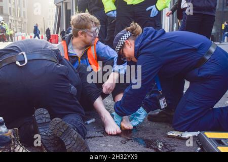 Londres, Royaume-Uni.25 octobre 2021.Les policiers dissolvent la colle sur les pieds d'un manifestant pendant la manifestation. Isolez les manifestants britanniques se sont collés sur la route et ont bloqué Wormwood Street et Bishopsgate, près de la gare de Liverpool Street.La manifestation est d’exiger du gouvernement qu’il isole toutes les maisons du Royaume-Uni d’ici 2030 afin de réduire les émissions de carbone.(Photo de Vuk Valcic/SOPA Images/Sipa USA) crédit: SIPA USA/Alay Live News Banque D'Images