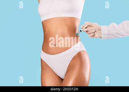 Procédure de beauté pour le corps parfait.Femme mince ayant un traitement de lipolyse à la clinique de salon de beauté.Chirurgien plastique en gants faisant l'injection au niveau du ventre a Banque D'Images