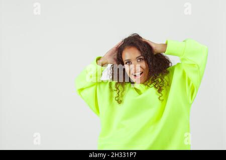 Jeune femme africaine portant un pull à capuche rose et un short de cyclisme blanc posé sur fond blanc.Look sportif décontracté pour femme Banque D'Images