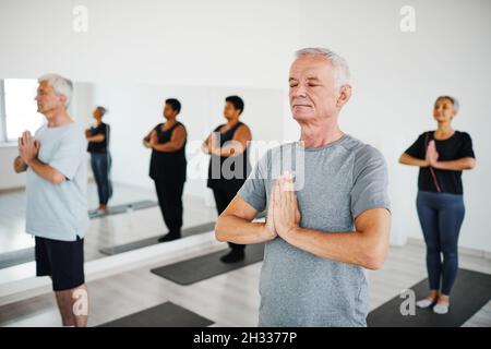 Groupe de personnes âgées debout sur des tapis avec leurs yeux fermés et méditant pendant l'entraînement en salle de gym Banque D'Images
