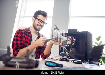 Portrait d'un sympathique homme qualifié et enjoué qui fixe la solution de sécurité détaillée d'un drone au poste de travail à l'intérieur Banque D'Images