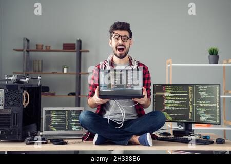 Portrait d'un adorable pirate informatique désespéré assis sur une table tenant une base de données de code d'ordinateur portable au poste de travail à l'intérieur Banque D'Images
