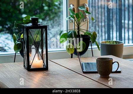 Travail à distance avec ordinateur portable et café en hiver avec lanterne aux chandelles sur table en bois pour créer une atmosphère confortable à l'intérieur. Banque D'Images