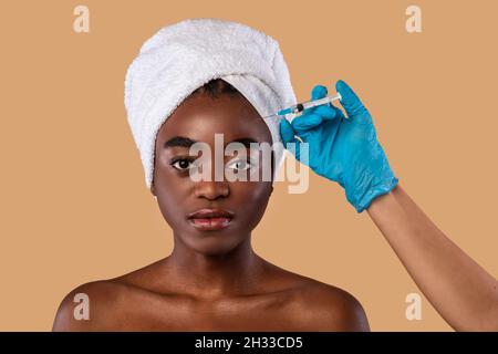 Concept de levage de la peau.Photo de la jeune femme noire dans le hijab recevant l'injection de remplissage de beauté dans le front debout isolé sur l'arrière-plan de studio.Doc Banque D'Images