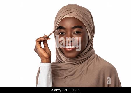 Concept de maquillage naturel.Attrayant bonne musulmane noire dame se brosser les sourcils tenir la brosse profiter de la routine de beauté du matin et regarder l'appareil photo.Fémal Banque D'Images