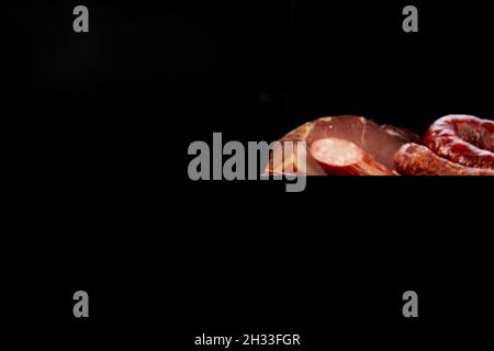 Prise de divers types de saucisses et de saindoux fumés sur une table sombre sur fond noir Banque D'Images