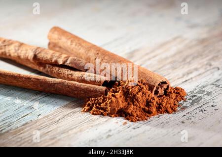 Gros plan de plusieurs bâtons de cannelle roulés avec de la poudre de cannelle en face d'eux sur une surface en bois avec des résidus de peinture. Banque D'Images