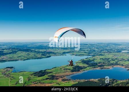 Des pilotes de parapente sur un paysage de lac en Bavière, devant un ciel bleu et une vue panoramique magnifique. Banque D'Images