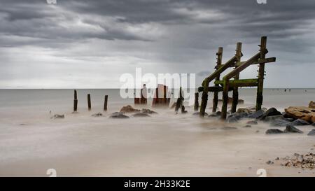 Les remins des défenses marines sous les falaises rapidement érodées de Happisburgh (Haisbro) sur la côte nord de Norfolk s'élèvent comme des sentinelles de la mer. Banque D'Images