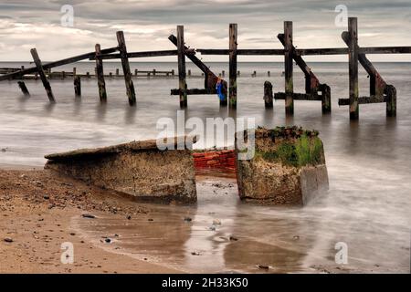 Les remins des défenses marines sous les falaises rapidement érodées de Happisburgh (Haisbro) sur la côte nord de Norfolk s'élèvent comme des sentinelles de la mer. Banque D'Images