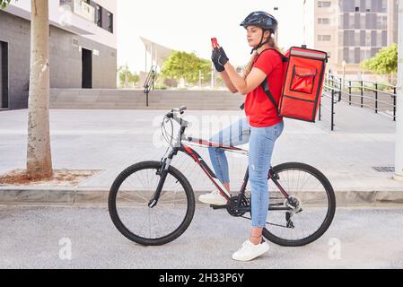 Une fille de livraison cycliste vérifie l'adresse de son prochain envoi avec son téléphone portable Banque D'Images