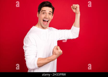 Photo portrait brunet dans des vêtements blancs gestants comme le gagnant souriant isolé couleur rouge vif arrière-plan Banque D'Images