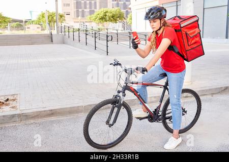 Une fille de livraison cycliste vérifie l'adresse de son prochain envoi avec son téléphone portable Banque D'Images