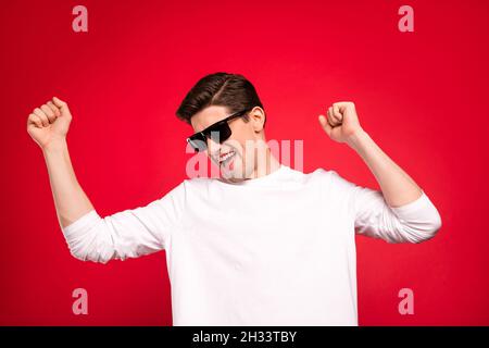 Photo portrait brunet gars dans une tenue décontractée portant des lunettes de soleil dansant à la fête isolé couleur rouge vif fond Banque D'Images