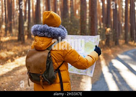 Jeune femme randonneur dans une veste chaude orange.Une femme marche dans un parc de pins d'automne avec un sac à dos.Elle regarde la carte qu'elle tient entre ses mains.Hik Banque D'Images