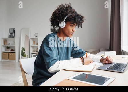 Portrait de vue latérale d'un adolescent afro-américain étudiant à la maison ou dans un dortoir d'université et utilisant un ordinateur portable, espace de copie Banque D'Images
