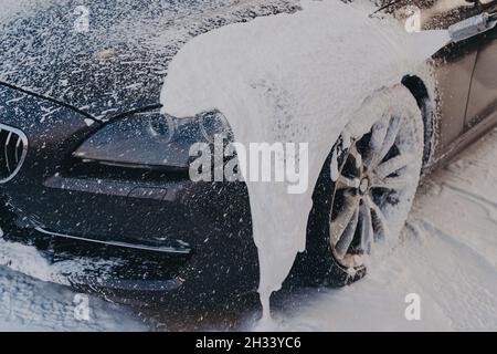 Voiture noire en mousse de savon blanc au poste de lavage Banque D'Images