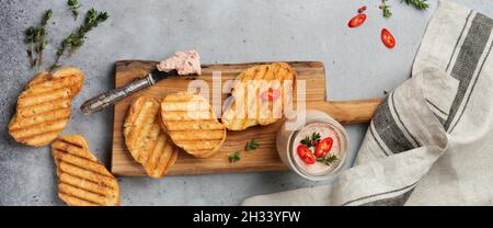 Pâté de foie fait maison au poulet avec poivre rouge, brindilles de thym et tranches de pain grillées sur un vieux panneau en bois sur fond de béton gris ou de pierre.Sélection Banque D'Images