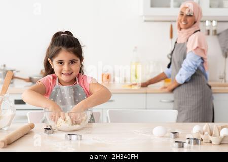 Adorable petite fille pétriant de la pâte dans la cuisine pendant que son maman de nettoyage sur le fond, jolie femme enfant d'apprendre à cuire des biscuits, appréciant passer du temps Banque D'Images