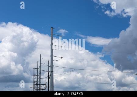 Vue sur les sommets de plusieurs poteaux électriques métalliques, chacun portant plusieurs lignes, contre un ciel bleu avec des nuages blancs, aspect horizontal Banque D'Images