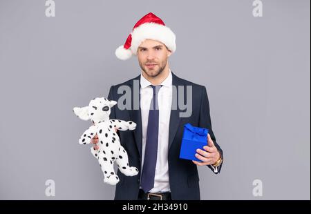 homme d'affaires en chapeau de père noël, boîte cadeau et jouet sur fond gris, vacances de noël Banque D'Images