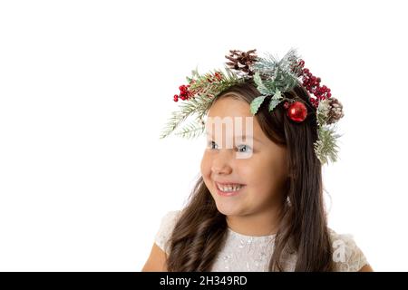 Portrait en gros plan de l'enfant, fille intéressée dans la couronne de Noël des branches de sapin, des cônes et des jouets d'arbre de Noël regarde loin avec l'espace de copie, isolé sur Banque D'Images