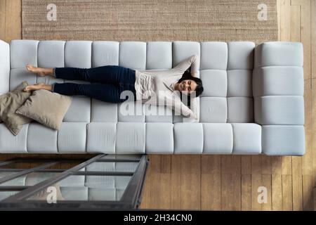 Heureuse femme asiatique paresseuse satisfaite se relaxant sur un grand canapé confortable Banque D'Images