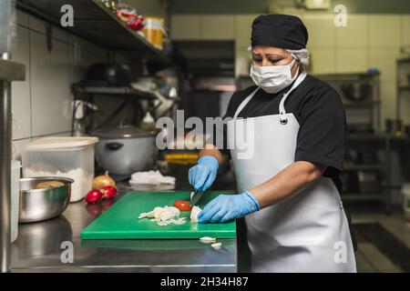 Faire cuire les oignons coupés sur une planche en plastique dans la cuisine du restaurant Banque D'Images