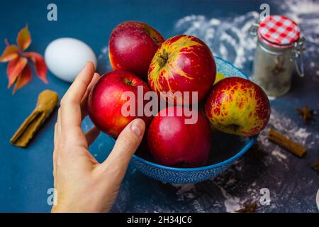 La main d'une femme atteint une pomme rouge mûre dans un bol.Choisir des produits pour faire une tarte aux pommes traditionnelle de Thanksgiving.Ingrédients pour cuire à la maison. Banque D'Images