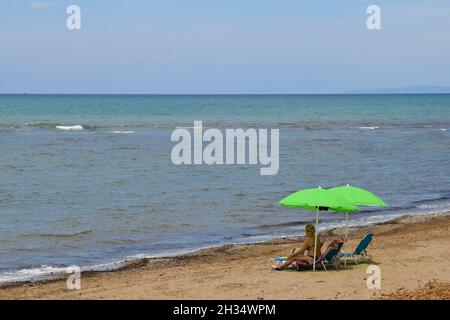 Une plage de sable avec une femme sous des parasols sur le bord de mer de la côte toscane en été, San Vincenzo, Livourne, Toscane, Italie Banque D'Images