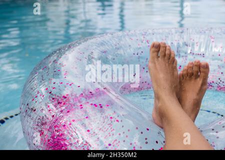 Pieds de femme sur un anneau en caoutchouc avec paillettes dans la piscine, à proximité.Femme se détendant près de la piscine. Banque D'Images