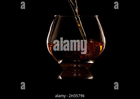 Verser le whisky dans un verre rocailleux sur fond noir Banque D'Images