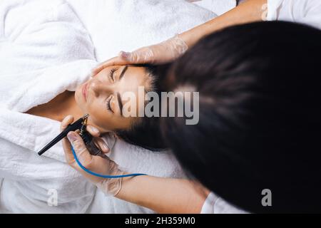 Le cosmétologue effectue une procédure de gommage de l'eau sur les joues du client.Procédure de beauté de cosmétologie.Concept de rajeunissement du visage, cosmétologie. Banque D'Images