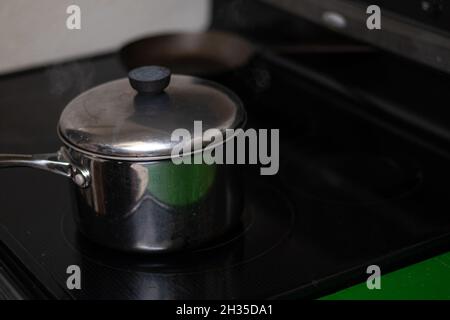 Cuiseur vapeur avec couvercle sur une cuisinière noire. Banque D'Images
