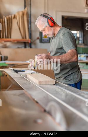 Travailleur mesurant une marche en bois sur une scie à table coulissante Banque D'Images