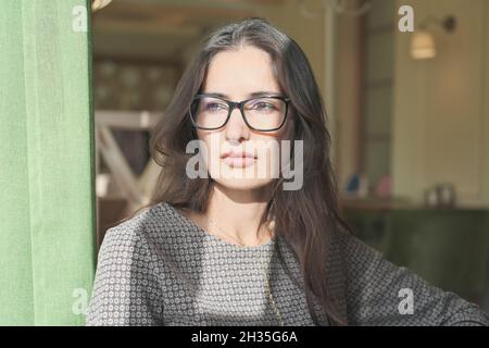 femme de course asiatique mixte assise dans un café et regardant de côté. jeune femme d'affaires belle portant des lunettes pensant seule. femme calme et réfléchie avec humour Banque D'Images