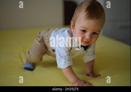 Joli petit bébé assis sur le lit portant une chemise avec noeud papillon Banque D'Images