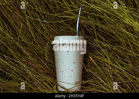 Une tasse à boisson réutilisable et une paille réutilisable reposent sur l'herbe verte. Banque D'Images