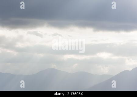 Blue mountains nuages rayons.La lumière du soleil à travers le brouillard illumine les pics.Espace de copie d'arrière-plan naturel atmosphérique.Calme neutre gris automne Banque D'Images