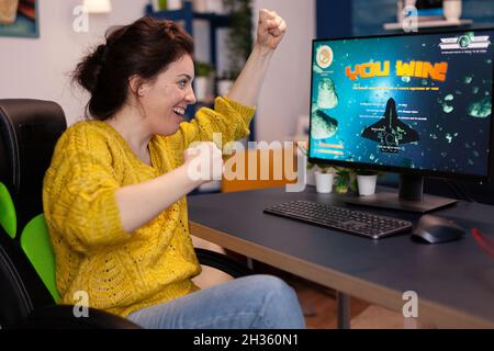 Excitée joueuse de compétition femme gagnant jeux vidéo de tir d'espace pendant le championnat de jeu en ligne dans le salon à la maison.Joueur effectuant un tournoi de cybersport.Victoire des jeux vidéo Banque D'Images