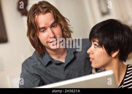 Joyeux jeune homme caucasien et femme multiethnique utilisant l'ordinateur portable ensemble. Banque D'Images