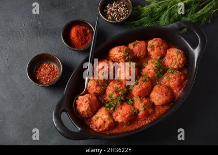 Boulettes de poisson, boulettes de poisson frites à la sauce tomate dans un plat noir sur une table en béton avec ingrédients Banque D'Images