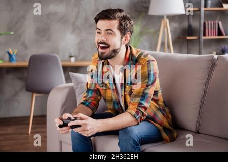 Photo de choqué funky jeune gars porter tenues décontractées assis canapé jouer jeu playstation indoor House room Banque D'Images