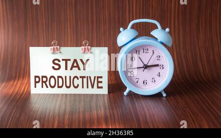 Restez productif, avec du texte sur l'autocollant et un arrière-plan en bois grâce au réveil bleu Banque D'Images