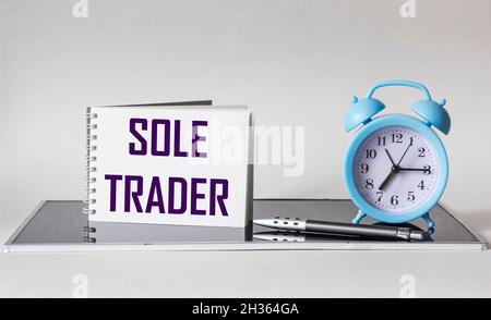 COMMERÇANT UNIQUE, texte sur bloc-notes blanc sur fond noir et blanc avec horloge et stylo Banque D'Images