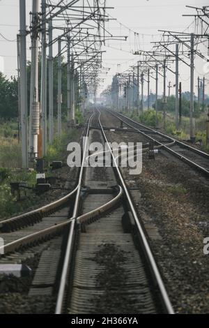 Cluj-Napoca, Roumanie, 7 juin 2009: Les voies ferrées convergentes vont jusqu'à un point de fuite à l'horizon avec des pôles de tension le long du côté. Banque D'Images