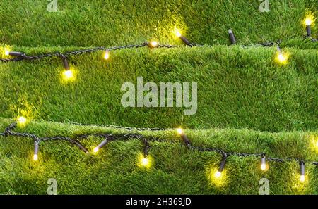 Arrière-plan inhabituel de l'arbre de Noël fait d'herbe artificielle décorée avec des guirlandes dorées.Mise au point sélective. Banque D'Images